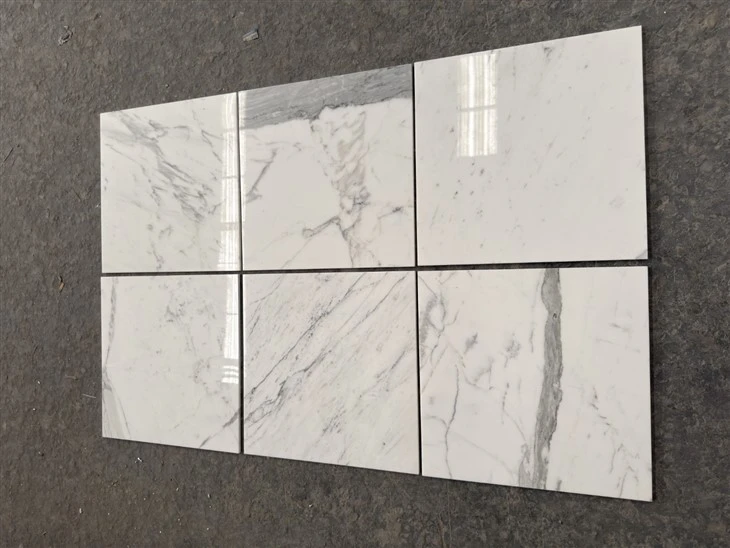 Close-up of polished Calacatta marble tiles arranged in a random-vein dry layout.